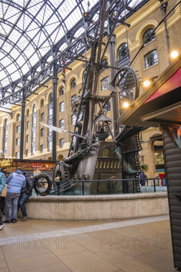 A large metal sculpture in a covered interior surrounded by people, The Navigators, London, United Kingdom