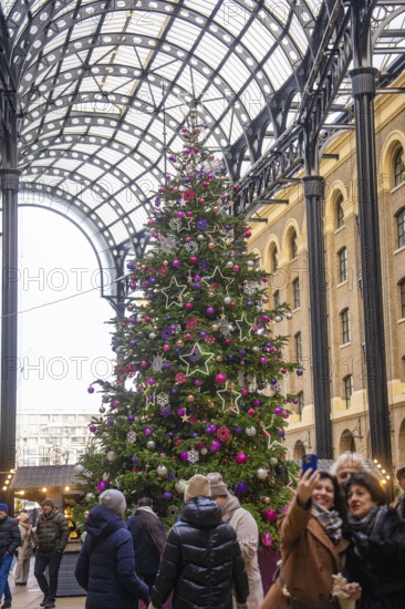 Large decorated Christmas tree in a lively interior with people taking pictures, London, United Kingdom