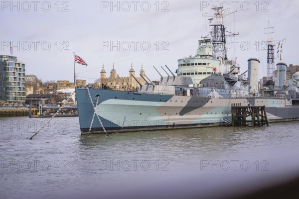 Historic warship on the riverbank in a city with British flag and buildings in the background, HMS Belfast, London, United Kingdom
