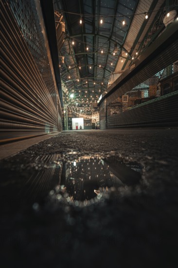 Puddle reflects lights in an urban canopy area at night, London, Borough Market, United Kingdom