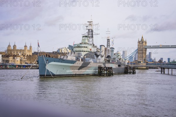 Large historic ship on the river in front of a bridge, with city skyline and towers on the horizon, HMS Belfast, London, United Kingdom