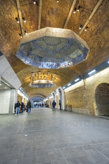 Long tunnel with decorative ceiling and people, warm lighting in an urban setting, London Bridge Station, London, United Kingdom
