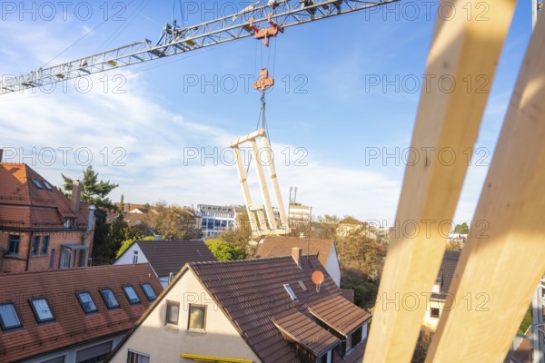 Construction crane transports timber elements over roofs on a construction site, carpentry, renovation, roof extension, Stuttgart, Germany
