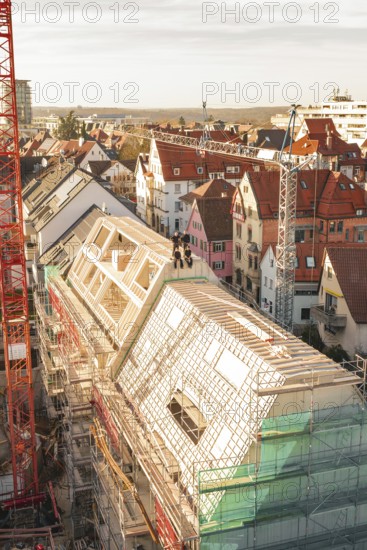 View of an active construction site with cranes, building scaffolding and long scaffolding along a roof in an urban environment, carpentry, renovation, roof extension, Stuttgart, Germany