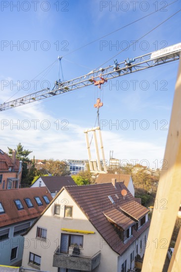 Wood element hanging from a crane over a roof with a clear sky, carpentry, renovation, roof extension, Stuttgart, Germany