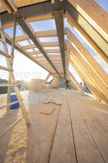 A construction worker works on an incomplete roof truss at sunrise or sunset, carpentry construction, roof extension, renovation, Stuttgart, Germany