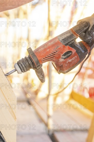 A construction worker operates a red drill on a construction site. Sunlight illuminates the scene, carpentry construction site, roof extension, renovation, Stuttgart, Germany