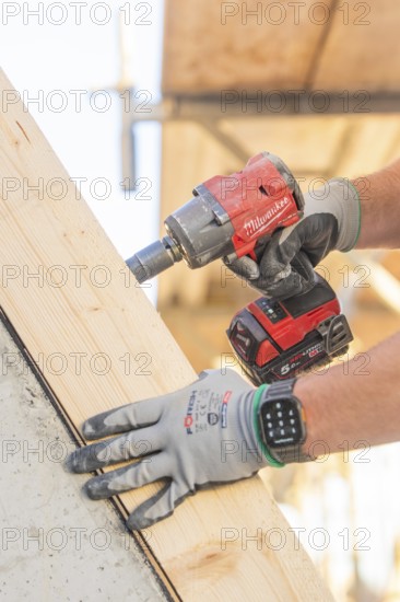 A worker with gloves uses a cordless screwdriver on a large piece of wood, carpentry construction, roof removal, renovation, Stuttgart, Germany