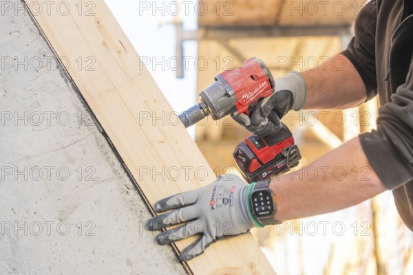 A worker with a cordless screwdriver fixing a piece of wood on a construction site, carpentry construction, roof removal, renovation, Stuttgart, Germany