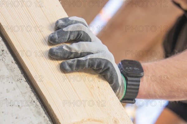 Close-up of a gloved hand holding a wooden plank, carpentry construction, roof extension, renovation, Stuttgart, Germany