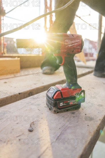A cordless screwdriver is lying on wooden scaffolding, illuminated by the evening sun, carpentry construction, roof extension, renovation, Stuttgart, Germany