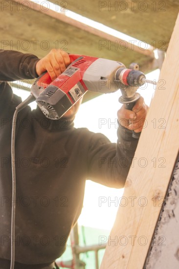 A worker uses a drill to process a slanted wooden board under sunlight, carpentry construction, roof extension, renovation, Stuttgart, Germany