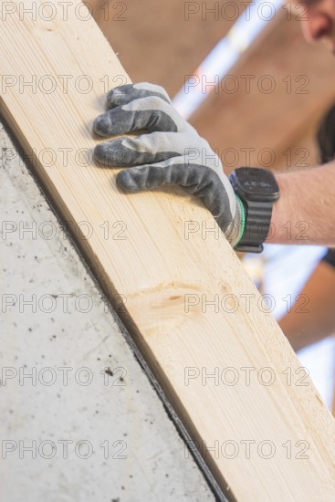 A gloved hand with a smartwatch holds a wooden board at a building, carpentry construction site, roof removal, renovation, Stuttgart, Germany