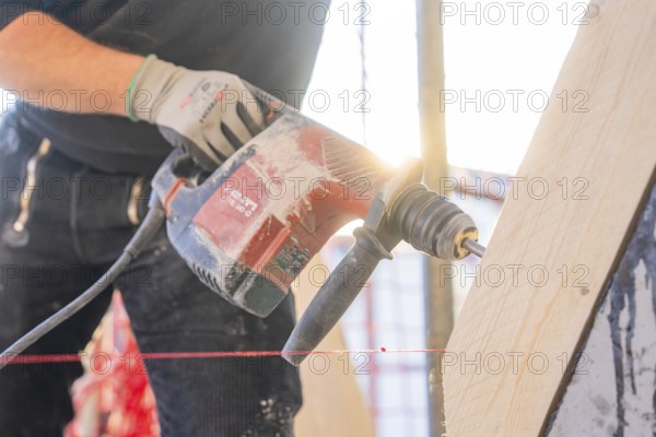 A worker with a red-black drill works on a wooden plank in sunlight, carpentry construction, roof extension, renovation, Stuttgart, Germany