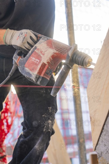 A worker is drilling wood with a red electric drill on a construction site. Dust flies up, carpentry construction site, roof extension, renovation, Stuttgart, Germany