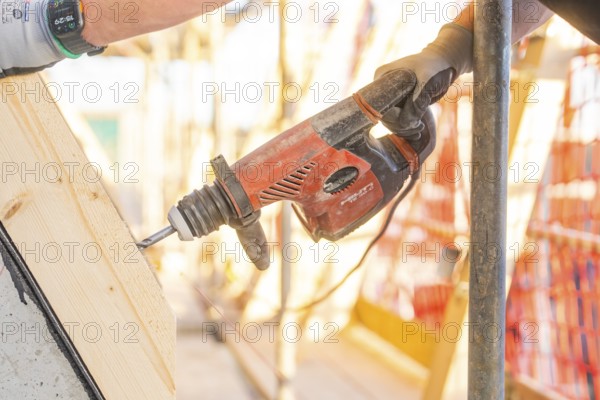 A worker drills into wood with a red drill while sunlight falls through the construction site, carpentry construction, roof extension, renovation, Stuttgart, Germany