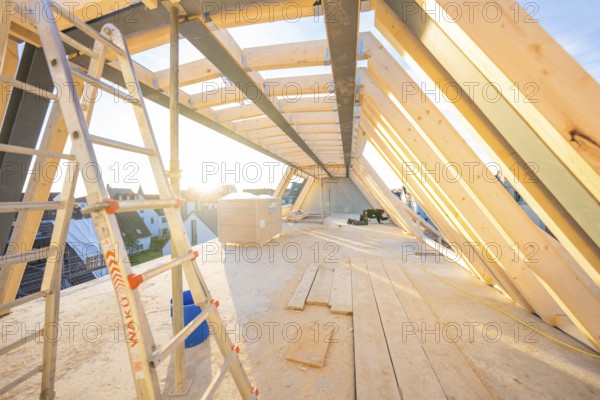 A half-finished roof truss with a ladder. Sunbeams illuminate the construction site, carpentry construction, roof extension, renovation, Stuttgart, Germany
