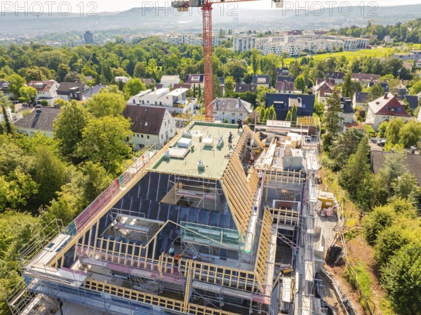 A new building with a construction crane in a residential area, surrounded by green vegetation and city views, carpentry construction, roof extension, renovation, Stuttgart, Germany