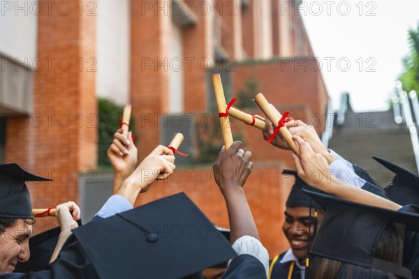 Diverse group of university students wearing graduation caps and gowns, celebrating their achievement and success while holding their diplomas joyfully in the air after completing their education