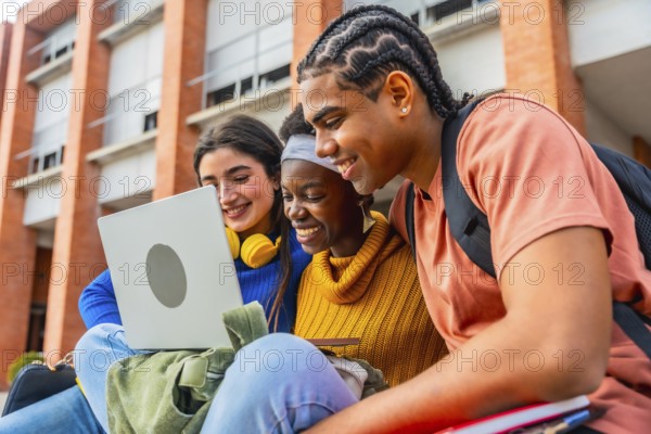 Group of happy young diverse students collaborating on a project, smiling and looking at a laptop computer outdoors at a university, highlighting teamwork and modern education