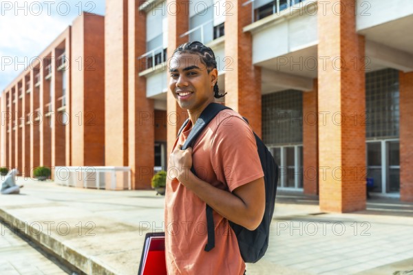 Young hispanic man student standing outdoors at university campus, wearing a backpack and holding folders, smiling and looking confident about his education and future