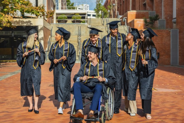 Diverse group of university graduates, including a man in a wheelchair, standing together on campus holding diplomas, celebrating their academic achievement and inclusion