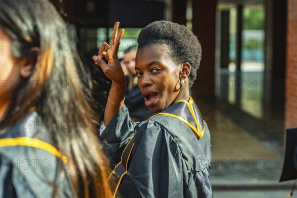 Young black woman in a graduation gown celebrating academic achievement, looking back at the camera and making a gesture of success, feeling excited about her future and education