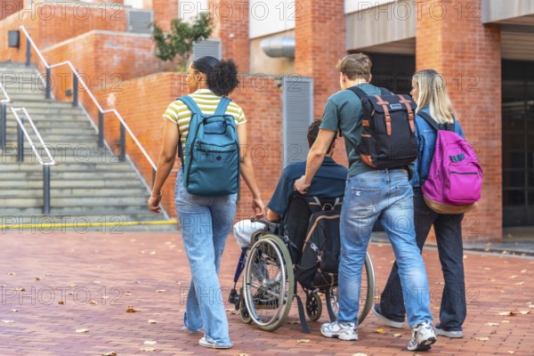 Group of diverse university students walking together on campus, one male student pushing a friend in a wheelchair while another female student walks beside them, showing support and inclusion