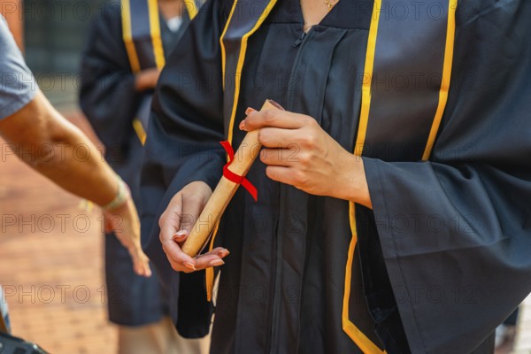 Graduate student is holding a rolled diploma tied with a red ribbon, celebrating academic achievement and the successful completion of their university education