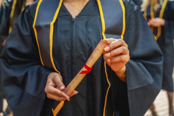 Graduate student is proudly holding a rolled diploma tied with a red ribbon, celebrating academic achievement and the completion of education during university graduation commencement