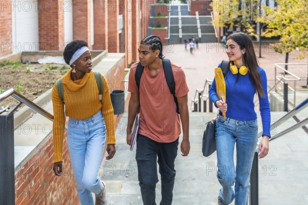 Diverse group of university students walking down outdoor stairs with books and backpacks, chatting and smiling on a modern campus in autumn, enjoying student life and friendship