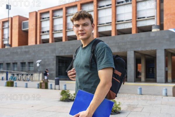 Young man student carrying a backpack and blue notebook, confidently walking on a modern university campus, representing education, learning, and the future of academic pursuit