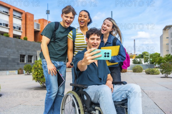 Group of happy young university students, including a man in a wheelchair, smiling and laughing while taking a selfie together outdoors on campus, celebrating friendship and inclusion