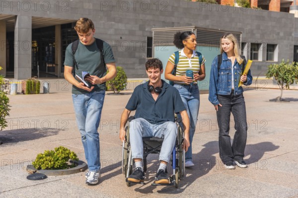 Group of four diverse university students walking on campus outdoors, one young man in a wheelchair smiling while interacting with friends showing inclusion and accessibility