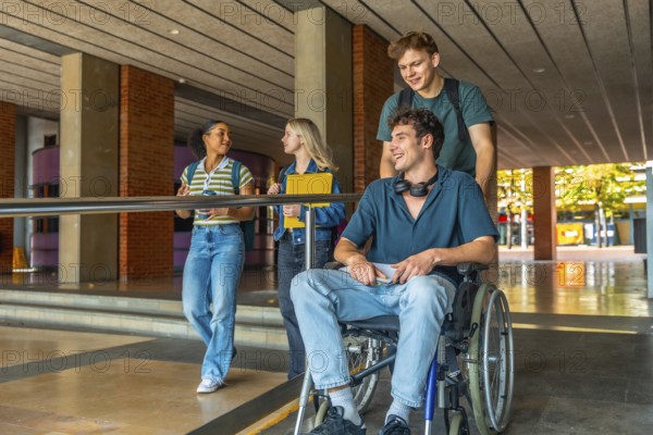 Diverse group of young adult university students walking and talking on campus, with one male student in a wheelchair being pushed by a friend, symbolizing inclusion and support