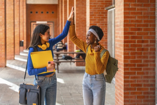 Two diverse university students celebrating academic success, high fiving and smiling happily while walking on campus, representing friendship and achievement in education