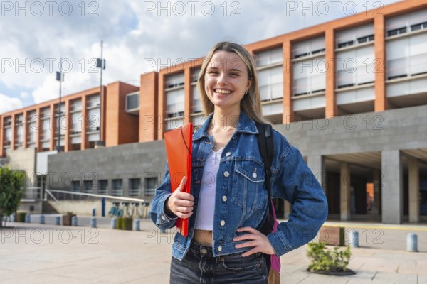 Happy young female student with backpack and folder smiling, standing in front of a modern university building, representing education, future, and academic life