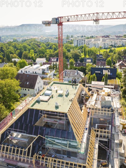A construction site with a crane over a roof, an urban and green landscape in the background, construction site of a carpentry workshop, roof extension, renovation, Stuttgart, Germany