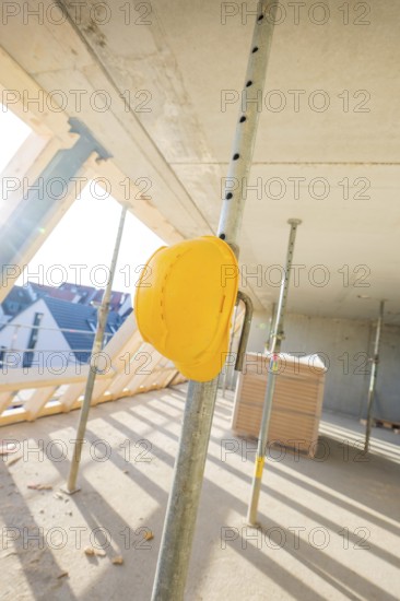 A yellow safety helmet hangs on a metal support on a construction site in sunlight, carpentry construction, roof extension, renovation, Stuttgart, Germany
