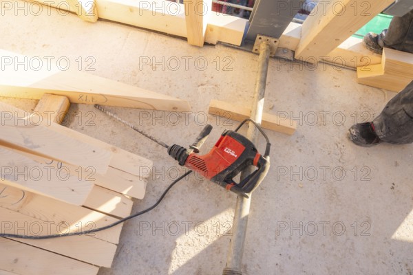 A drill is lying on a construction site floor, surrounded by wooden planks and a pair of shoes, carpentry construction, roof extension, renovation, Stuttgart, Germany