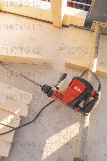 A red drill is lying on a concrete floor between wooden planks in bright surroundings, carpentry construction, roof extension, renovation, Stuttgart, Germany