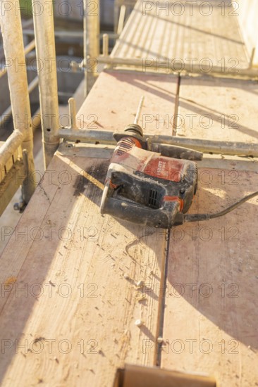 An electric drill is lying on wooden planks of scaffolding under bright sunlight, carpentry construction, roof extension, renovation, Stuttgart, Germany