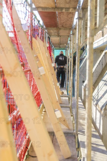 A worker walks over scaffolding surrounded by wooden boards and a protective net in a bright environment, carpentry construction, roof extension, renovation, Stuttgart, Germany