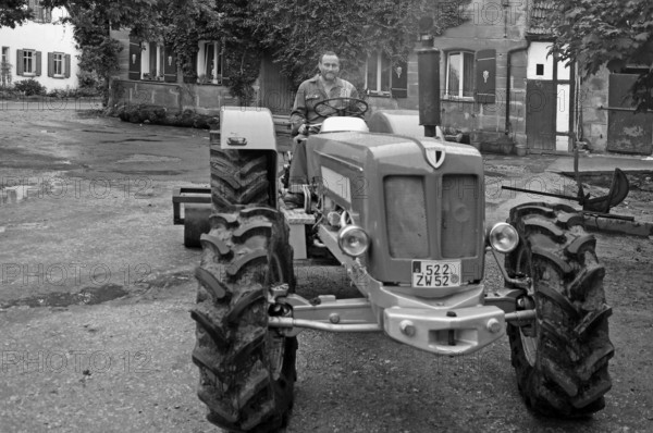 Farmer on his new Schlüter tractor in the yard, black and white, Tauchersreuth, Middle Franconia, Bavaria, Germany