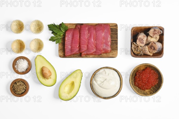 Colorful ingredients on a white surface, including sliced salted tuna, canned tuna, avocado, red caviar, and garnishes. This setup is ideal for making a delicious tuna tartare meal