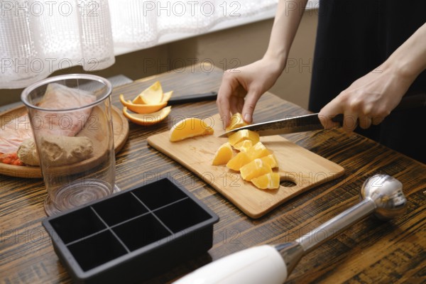 A person is cutting fresh oranges on a wooden board in a kitchen. The sunlight is coming through the window. Various kitchen tools are on the counter