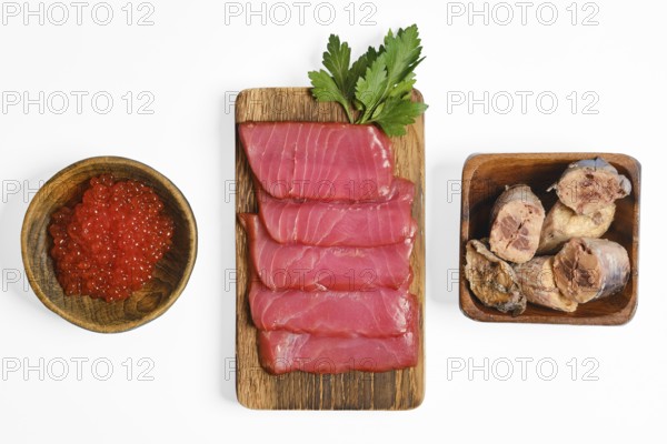 Sliced cured tuna fillets and canned tuna are on a wooden board, accompanied by a bowl of red fish roe