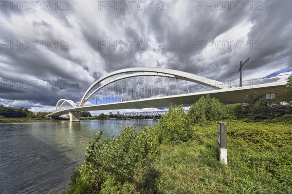 Beatus-Rhenanus Bridge, architect Marc Barani, pedestrian and tram bridge, Rhine river, border between Germany and France, border river, riverbank, catenary masts, overhead lines, trees, bushes, grass, blue partly cloudy sky, cumulus clouds, cumulus congestus clouds, image processing brightnesses and contrasts, Kehl, Upper Rhine Plain, Ortenau district, Baden-Württemberg, Germany