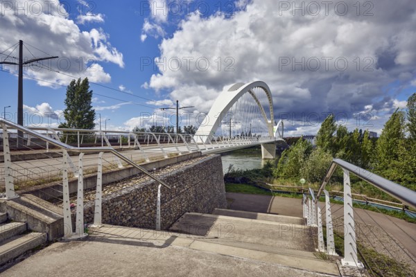 Beatus-Rhenanus bridge, architect Marc Barani, concrete staircase, stainless steel railing, catenary masts, overhead lines, pedestrian and tram bridge, Rhine river, grass, trees, partly cloudy blue sky, cumulus clouds, cumulus congestus clouds, Kehl, Upper Rhine plain, Ortenau district, Baden-Württemberg, Germany