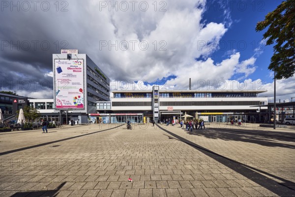 Train station, modern architecture, apartment building, concrete paving stone walkway, pedestrians as accessories, rainy weather, blue sky, cumulus congestus clouds, Am Bahnhofsplatz, Kehl, Upper Rhine Plain, Ortenau district, Baden-Württemberg, Germany